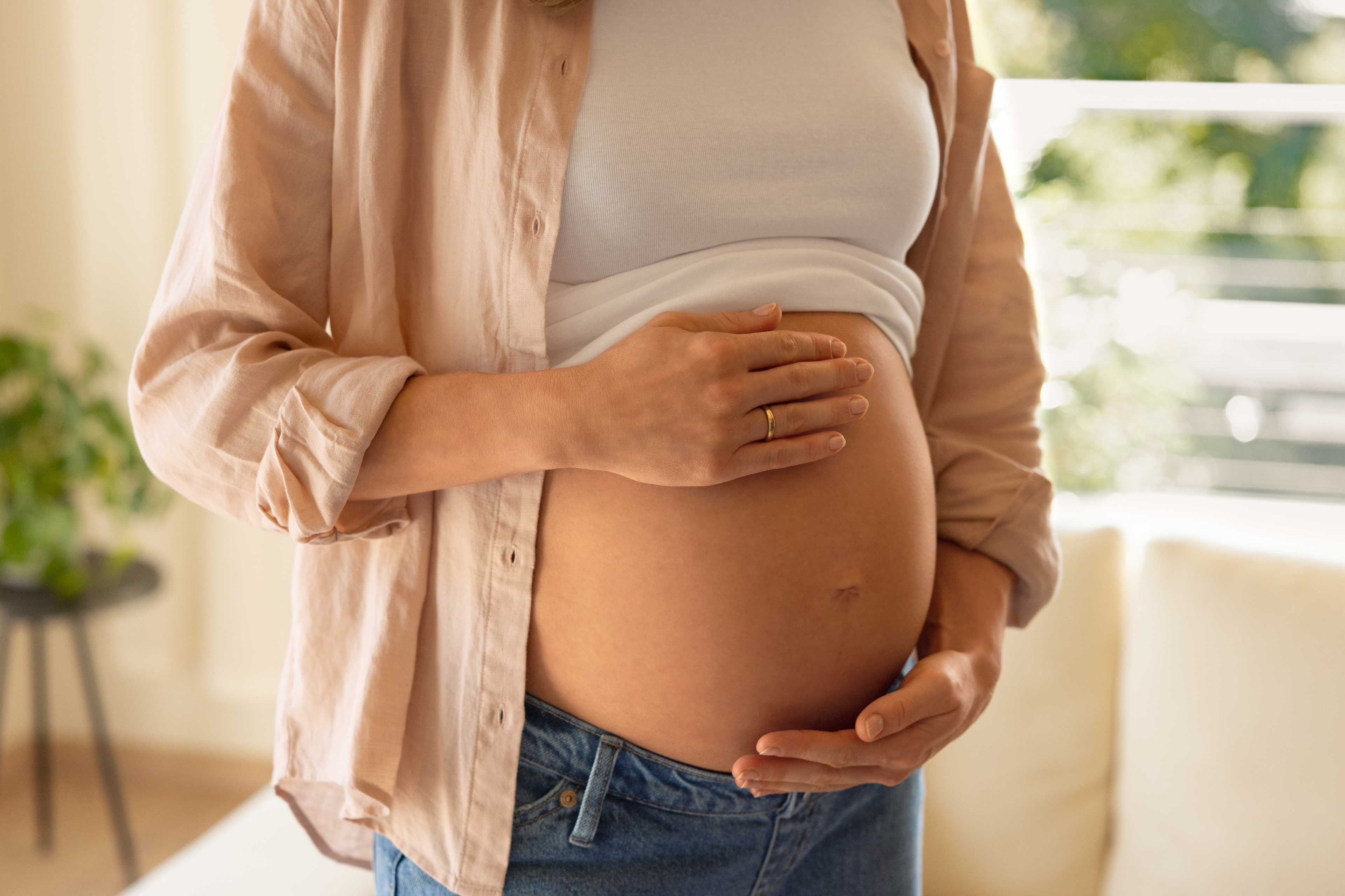 Schwangere Frau mit freiem Bauch, die ihre Hände schützend darauflegt