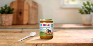HiPP Bio Babyglas Couscous-Gemüse-Pfanne ab 6. Monat auf Holztisch mit Löffel in heller Küchenumgebung