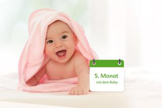 Baby liegt unter rosa Handtuch und stützt sich mit Armen nach vorne ab