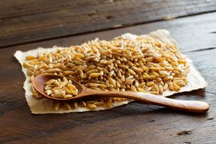 Ein mit goldfarbenen Körnern gefüllter Holzlöffel, der neben einem Haufen der gleichen Körner auf einer rustikalen Fläche liegt.