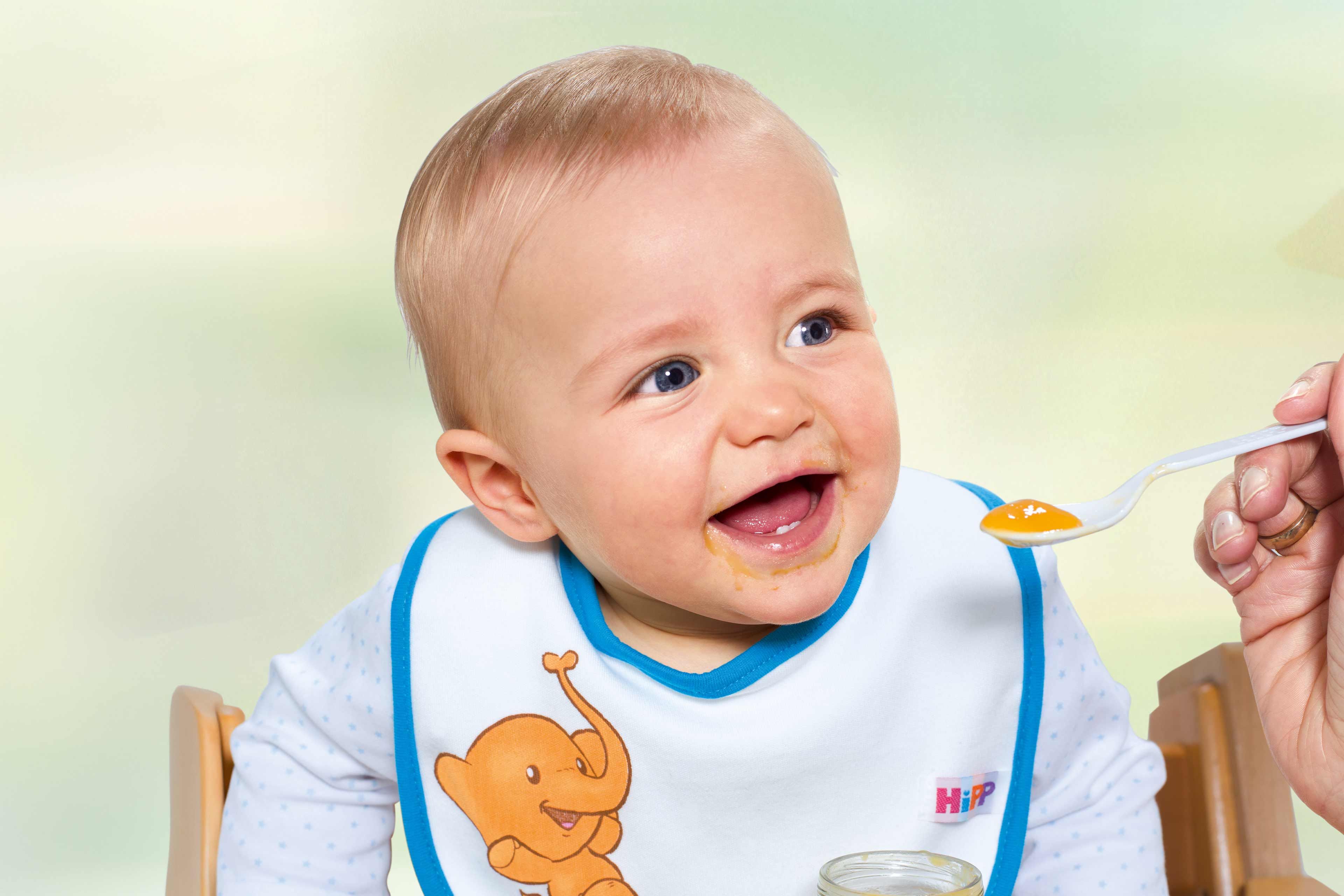 Kind im Hochstuhl und Lätzchen wird mit Babybrei gefüttert.