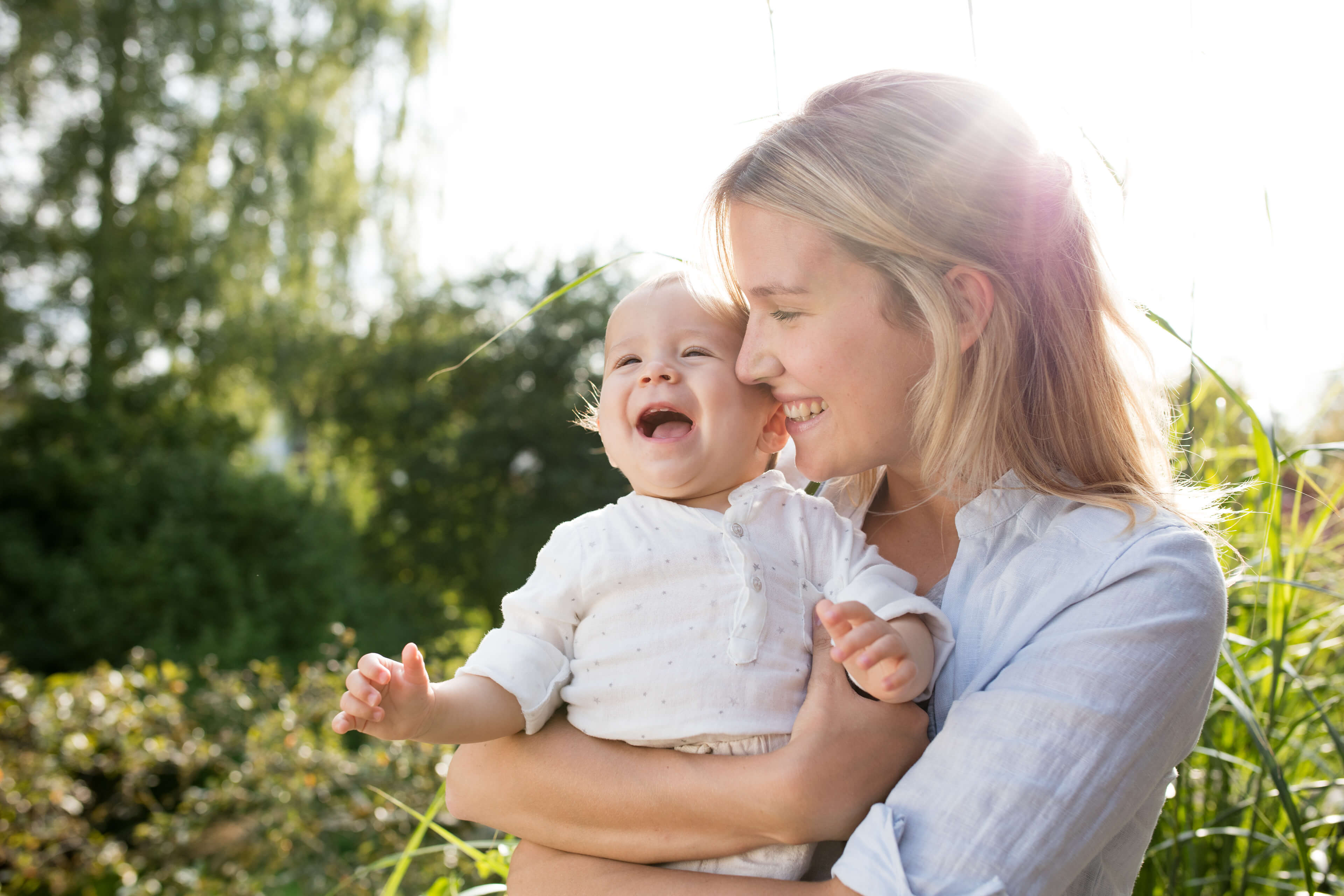 Ein zärtlicher Moment zwischen einer Mutter und ihrem Baby, wobei die Mutter ihr Kind im Arm hält und beide einen freudigen Moment inmitten einer natürlichen Kulisse erleben.