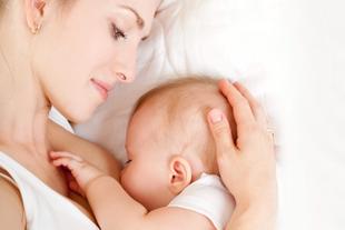Mutter liegt entspannt im Bett und stillt ihr Neugeborenes, während sie liebevoll den Babykopf hält.