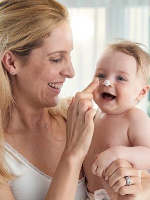 Frau hat Baby auf Arm und cremt ihm die Nase ein