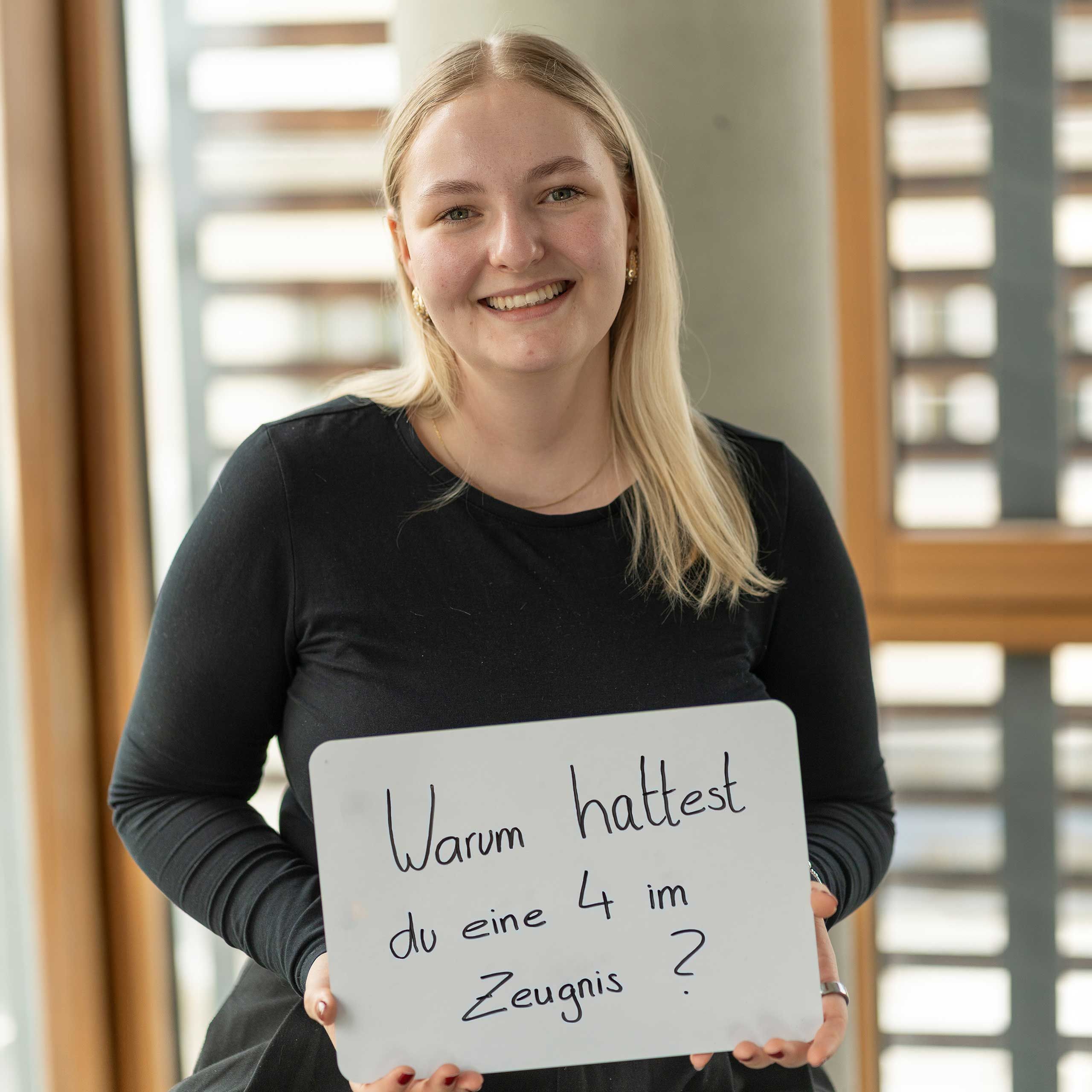 HiPP Mitarbeiterin hält ein Schild mit 'Warum hattest du eine 4 im Zeugnis?'