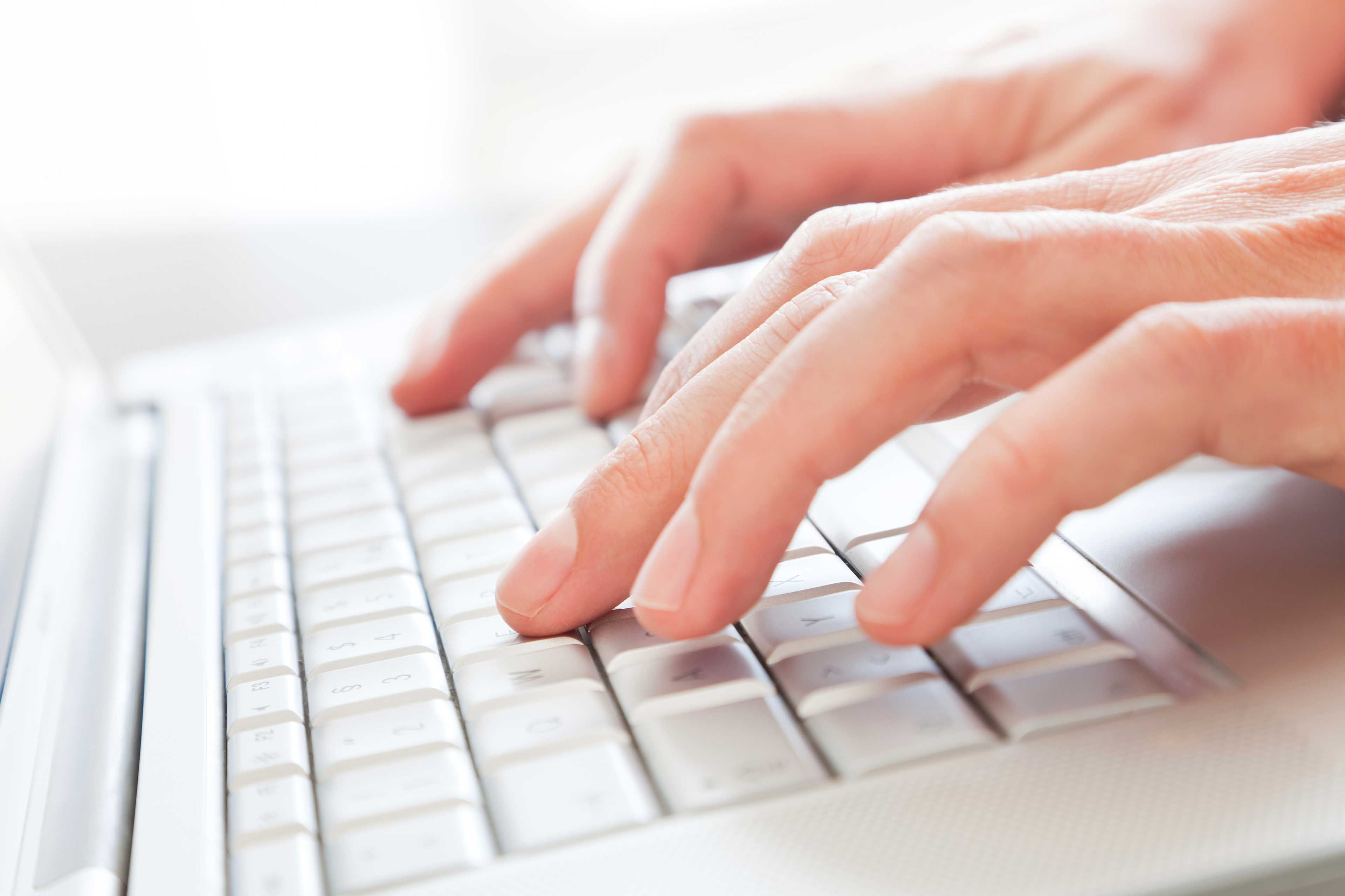 Hände tippen auf einer hellen Computertastatur, um eine barrierefreie Website-Erklärung zu verfassen.