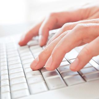 Hände tippen auf einer hellen Computertastatur, um eine barrierefreie Website-Erklärung zu verfassen.