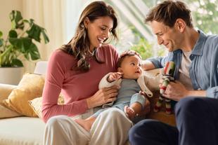 Lächelnde Eltern sitzen auf dem Sofa und kuscheln mit ihrem Baby – liebevoller Familienmoment im Alltag der Elternschaft