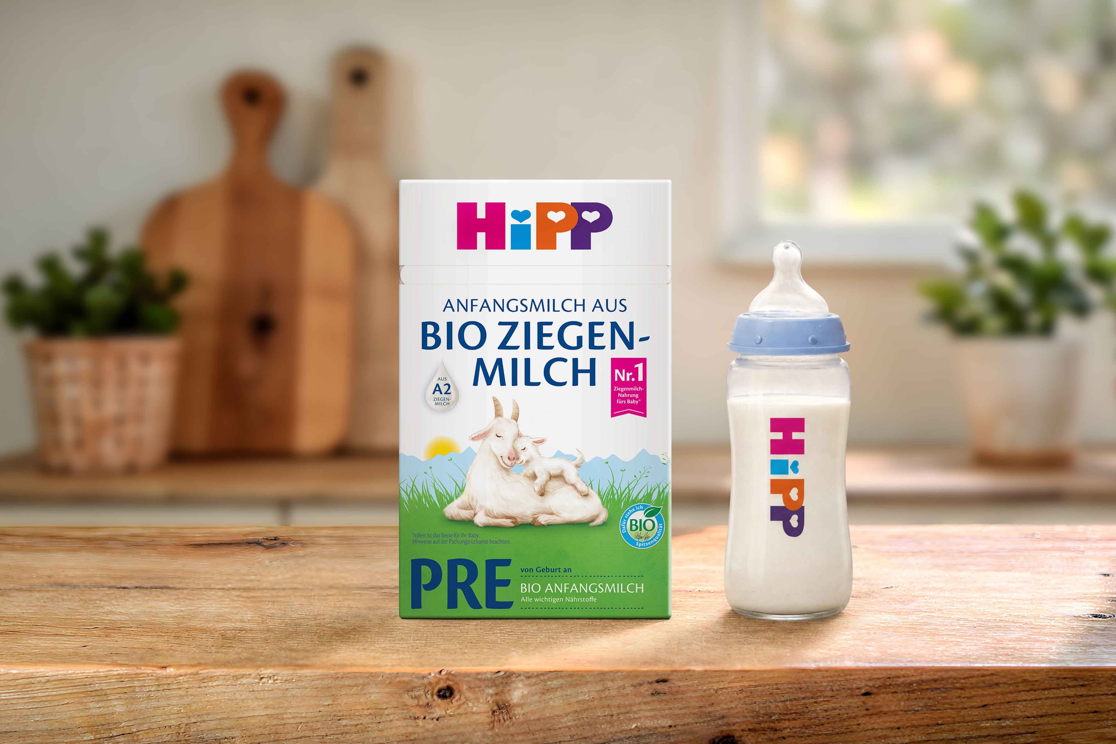 HiPP PRE Anfangsmilch aus Bio Ziegenmilch Packung mit Ziege und Zicklein neben gefülltem Fläschchen auf Holztisch in Küche