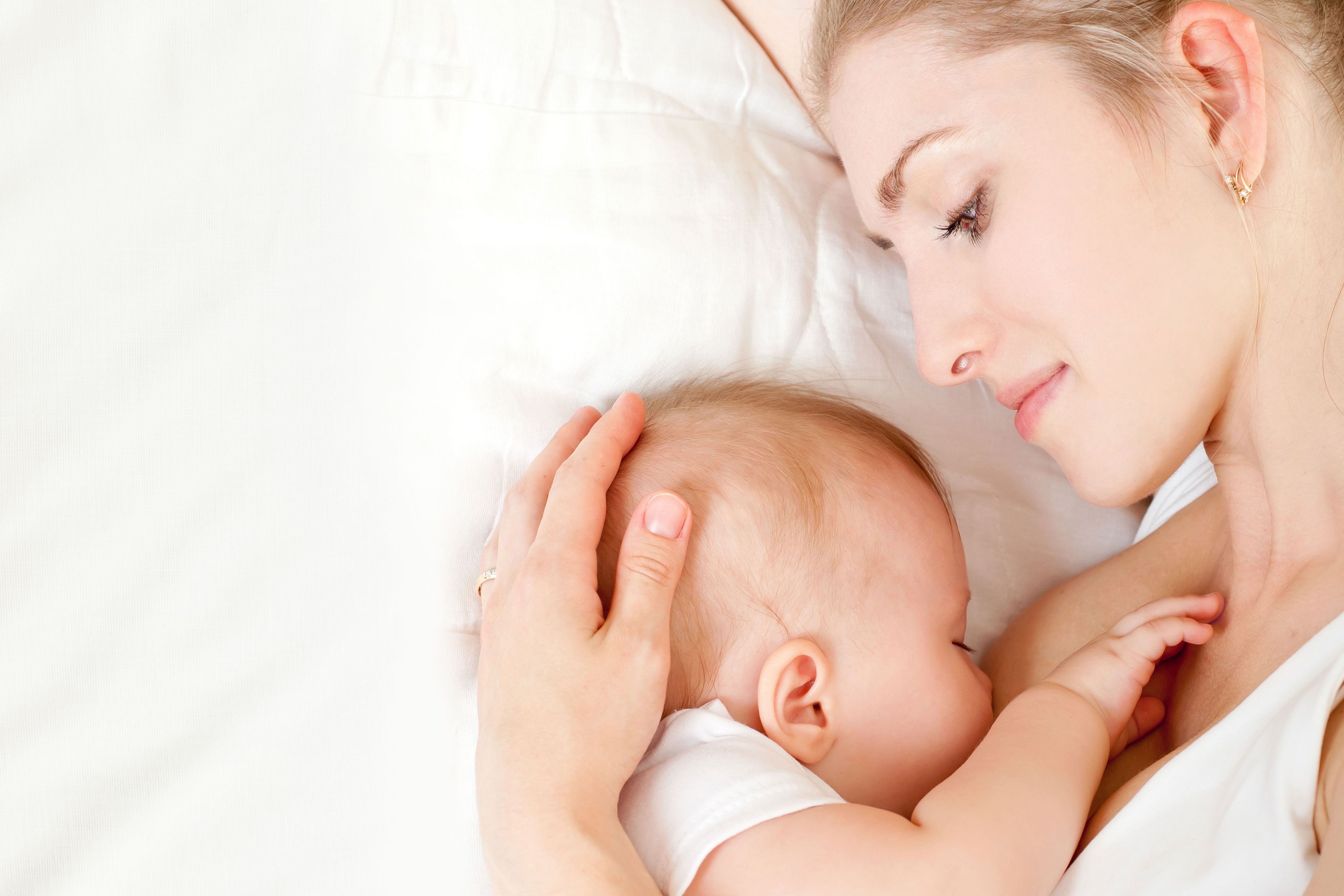 Ein zärtlicher Moment zwischen einer Mutter und ihrem Baby, in dem die Mutter sanft den Kopf des Babys hält und die beiden eine enge Bindung eingehen.