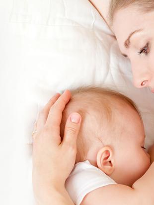 Ein zärtlicher Moment zwischen einer Mutter und ihrem Baby, in dem die Mutter sanft den Kopf des Babys hält und die beiden eine enge Bindung eingehen.