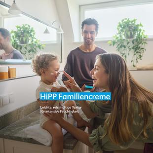 Mutter trägt einem lachenden Kleinkind im Badezimmer Creme auf, im Spiegel ist ein Mann zu sehen