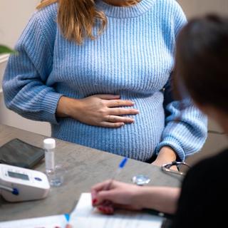 Pregnant woman in a blue jumper holding her bump while talking to a healthcare professional at a check-up.