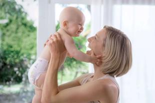 Ein freudiger Moment zwischen einer Mutter und ihrem Baby, wobei die Mutter das Baby hochhält und beide ein herzliches Lächeln teilen.