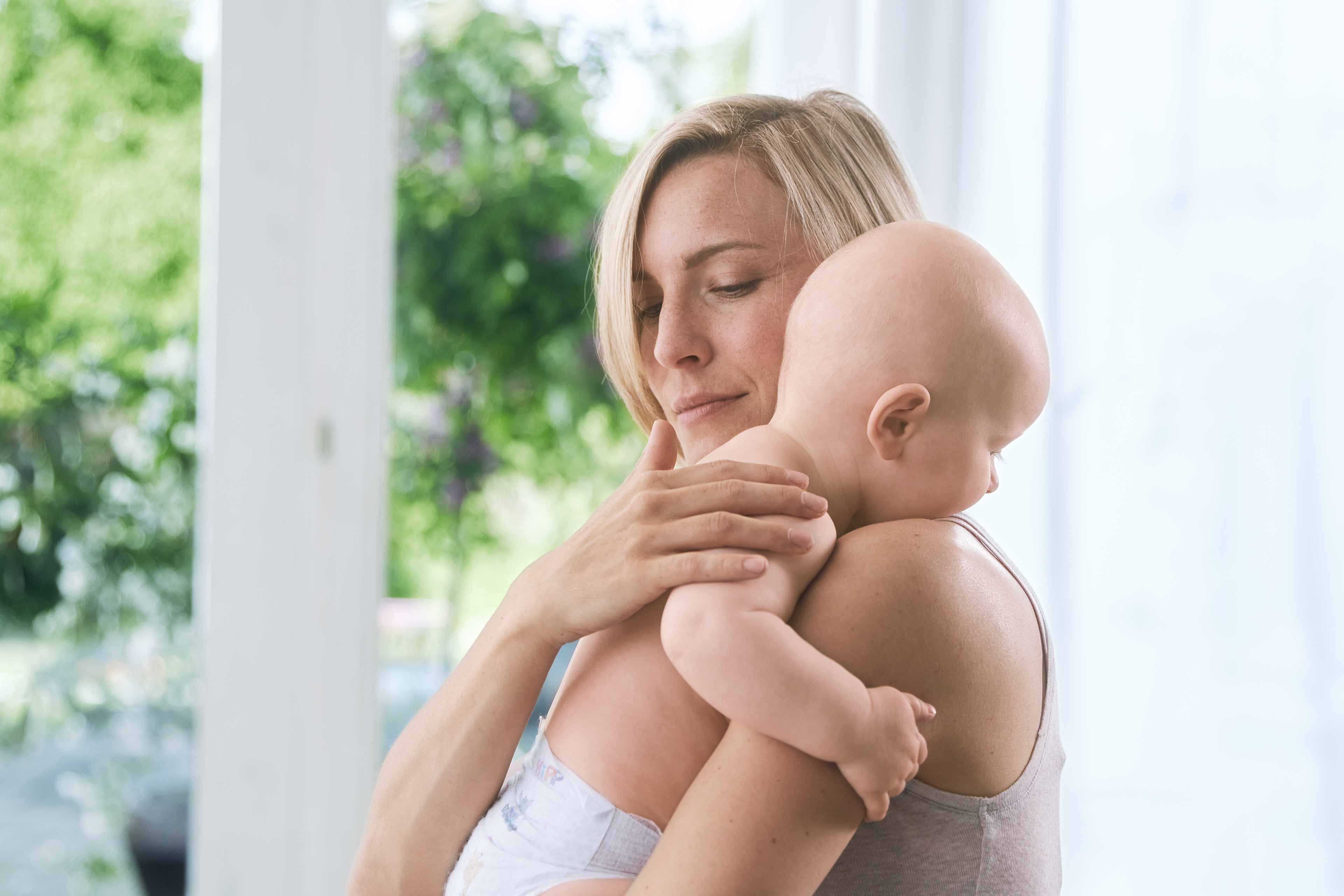 Eine Frau, die ein Baby an sich drückt, beide scheinen sich in einem ruhigen und intimen Moment zu befinden.