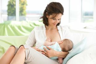 Mutter stillt ihr Baby entspannt in Wiegehaltung auf dem Sofa und unterstützt es sanft beim Anlegen während des Milcheinschusses