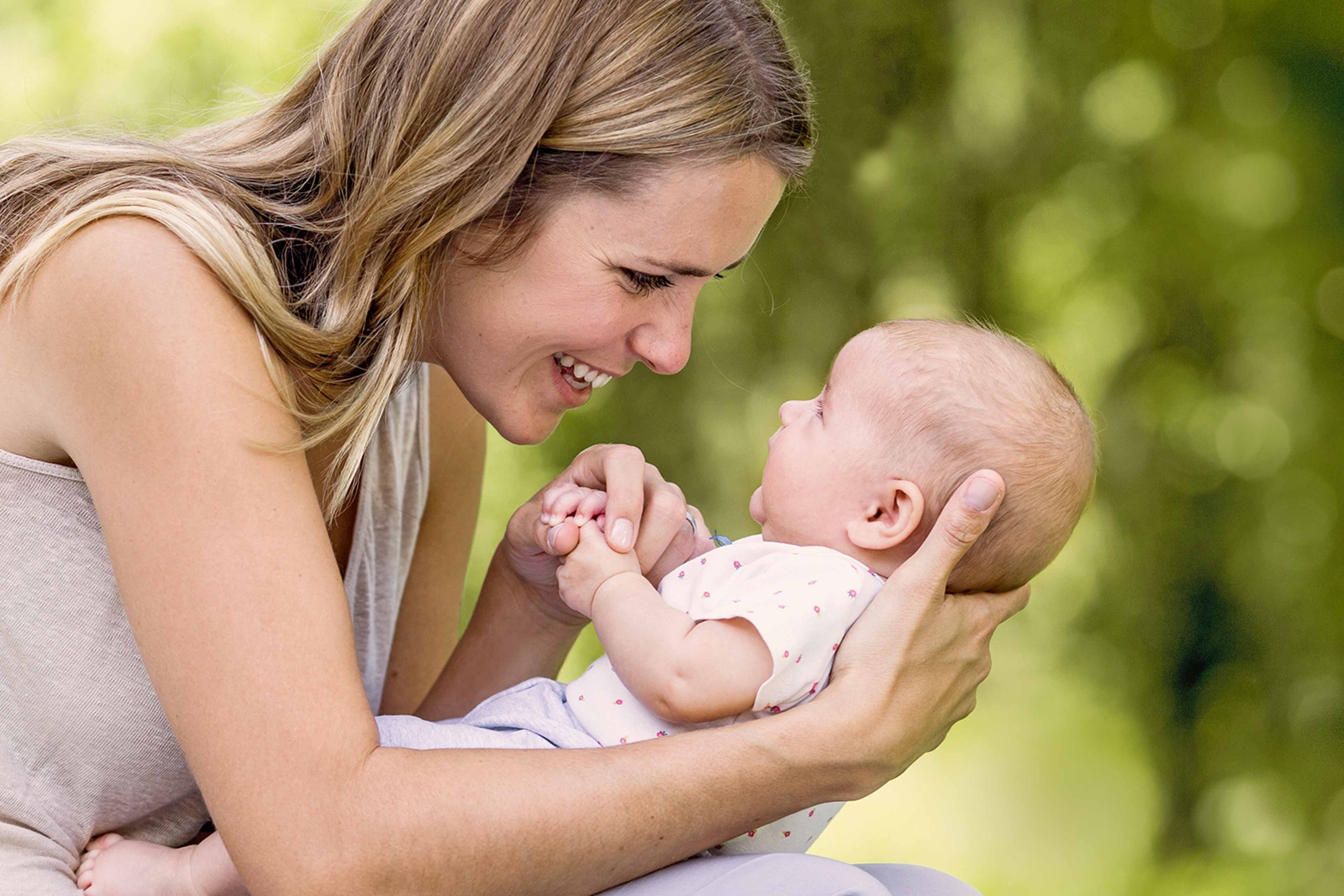 Ein zärtlicher Moment zwischen einer Frau und einem Baby, in dem die Frau das Baby im Arm hält und beide eine freudige Interaktion erleben.