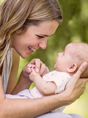 Ein zärtlicher Moment zwischen einer Frau und einem Baby, in dem die Frau das Baby im Arm hält und beide eine freudige Interaktion erleben.