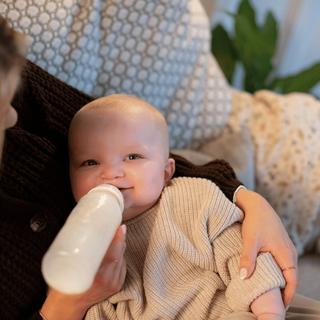 Smiling baby lying in a parent’s arms, being bottle-fed in a cosy, relaxed setting