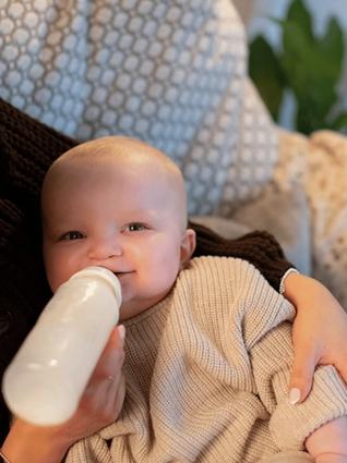 Smiling baby lying in a parent’s arms, being bottle-fed in a cosy, relaxed setting