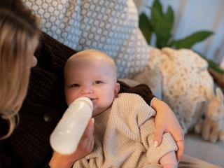 Smiling baby lying in a parent’s arms, being bottle-fed in a cosy, relaxed setting