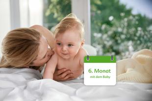 Mutter kuschelt mit ihrem etwa sechs Monate alten Baby auf dem Bett, daneben ein Kalenderfeld mit der Aufschrift „6. Monat mit dem Baby“.