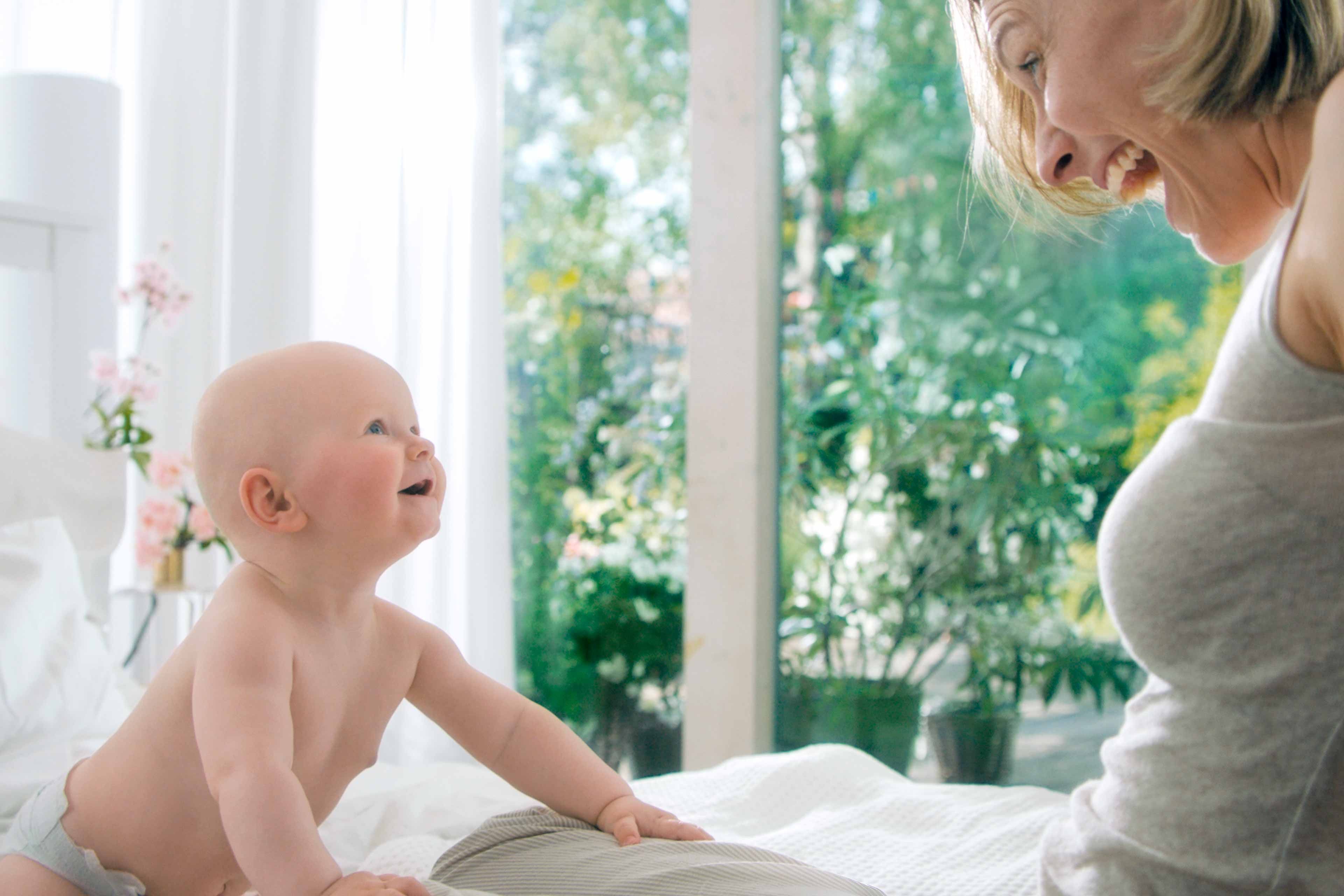 Ein herzerwärmender Moment zwischen einem Baby und einer Frau, wobei das Baby die Frau mit einem freudigen Gesichtsausdruck anschaut und die Frau ihrerseits das Baby anlächelt.