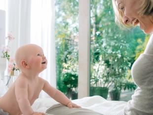 Ein herzerwärmender Moment zwischen einem Baby und einer Frau, wobei das Baby die Frau mit einem freudigen Gesichtsausdruck anschaut und die Frau ihrerseits das Baby anlächelt.