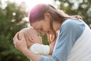 Ein zärtlicher Moment zwischen einer Mutter und ihrem Baby, in dem sie inmitten einer Naturkulisse einen intimen Blick miteinander teilen.