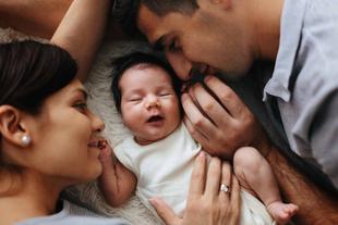 Ein zärtlicher Moment zwischen einer Mutter, einem Vater und ihrem neugeborenen Baby, das gemütlich zwischen ihnen ruht.