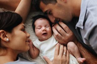 Ein zärtlicher Moment zwischen einer Mutter, einem Vater und ihrem neugeborenen Baby, das gemütlich zwischen ihnen ruht.