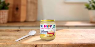 HiPP Guten Morgen Bio-Porridge Mango-Banane im Glas mit Löffel auf Holztisch in heller Küche
