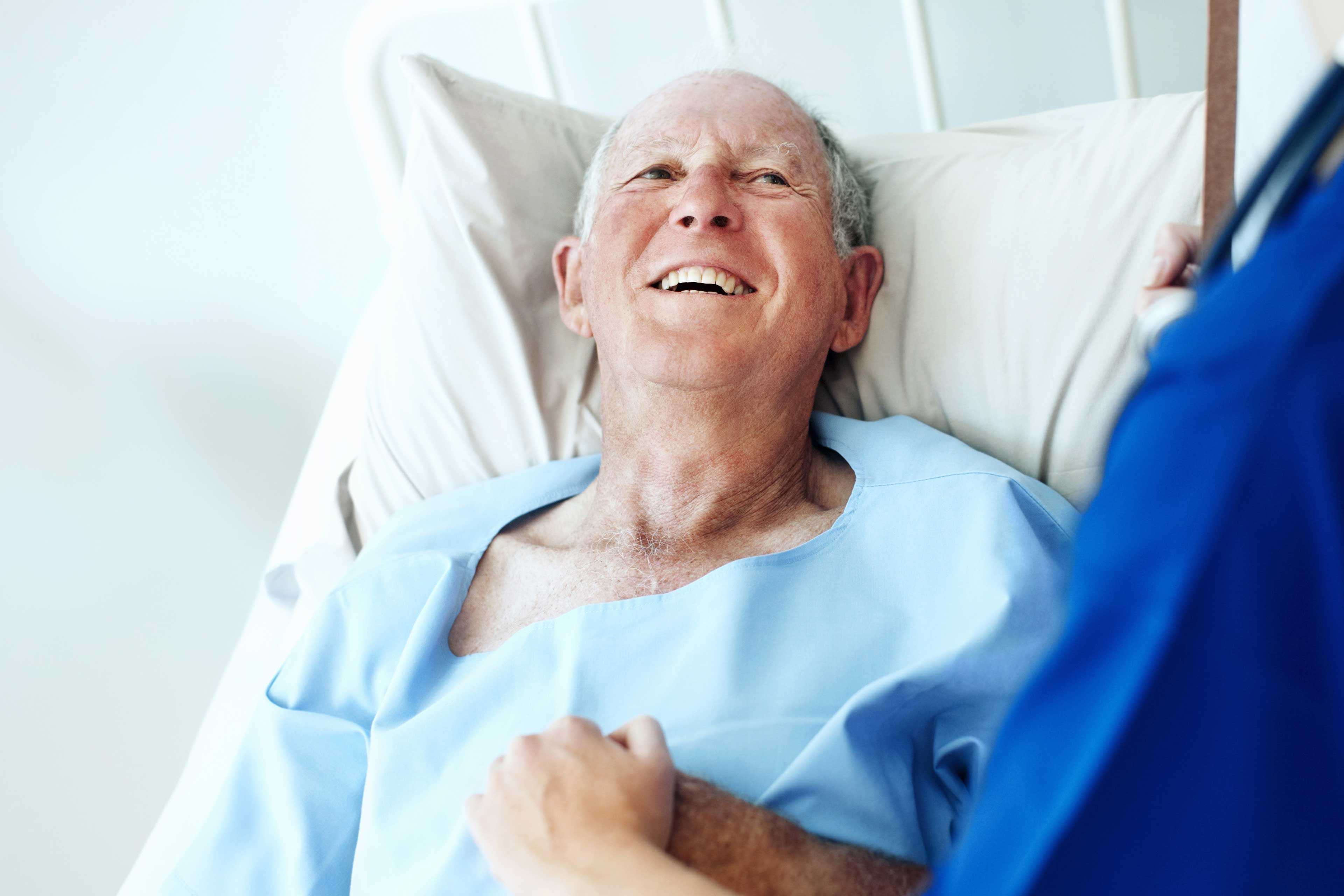 Älterer Mann liegt lächelnd im Krankenhausbett