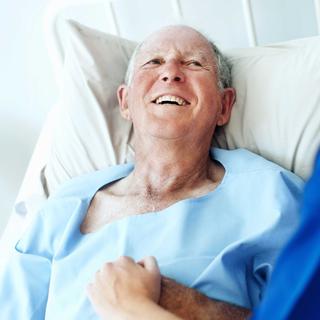 Älterer Mann liegt lächelnd im Krankenhausbett