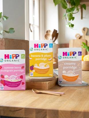 HiPP Organic baby cereals, including baby rice and porridges, displayed on a bright wooden kitchen worktop with plants.