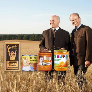 Zwei Männer im Getreidefeld neben historischen und modernen HiPP-Babygläschen, Sinnbild für die lange HiPP-Historie und Qualität.