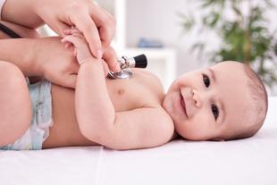 Ein auf dem Rücken liegendes Baby, bei dem eine medizinische Fachkraft mit einem Stethoskop den Herzschlag des Babys abhört.