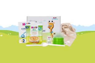 Mehrere Babynahrungsprodukte der Marke HiPP vor einer Geschenkbox mit Giraffenmotiv auf grün-blauem Hintergrund