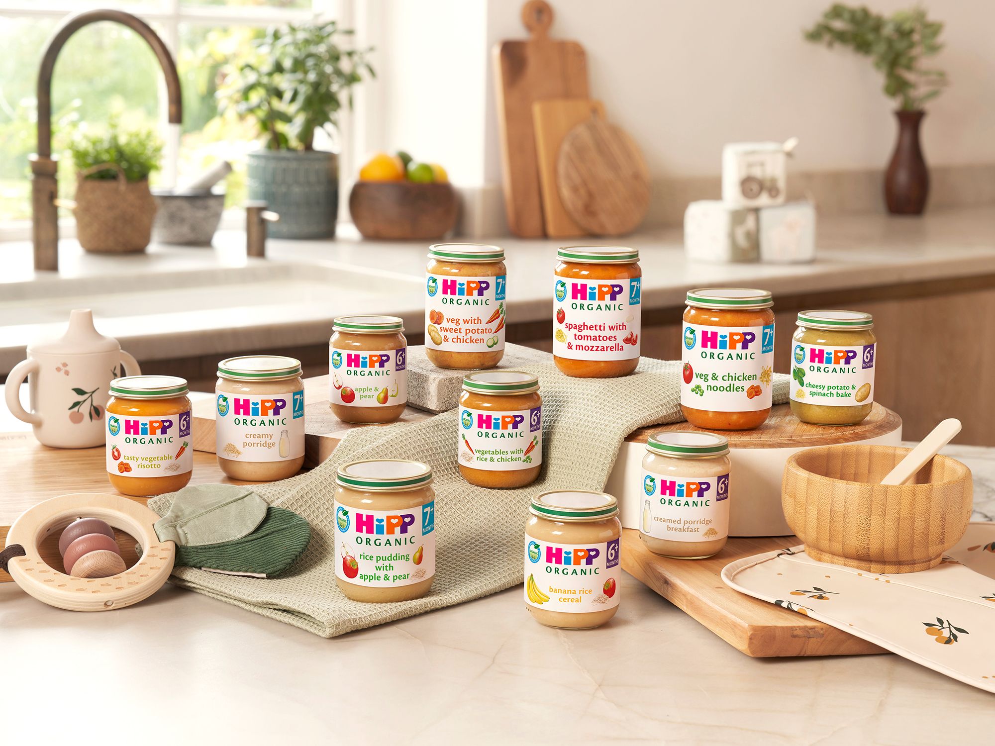 Selection of HiPP Organic baby food jars arranged on a cosy kitchen worktop, showing a variety of different flavours.