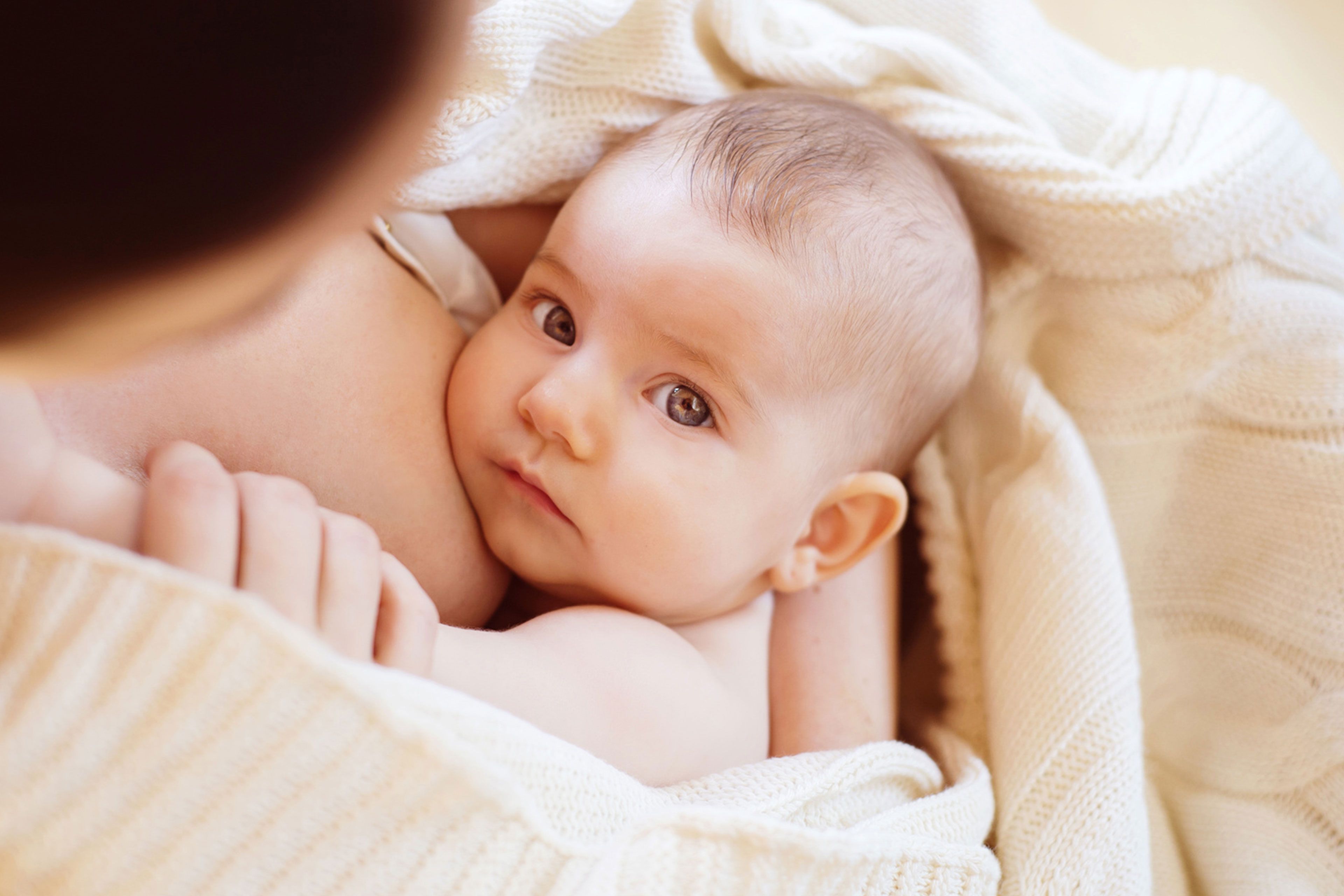Ein zärtlicher Moment zwischen einer Mutter und ihrem Baby, das mit neugierigem Blick direkt in die Kamera blickt.