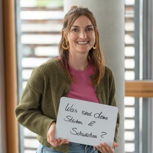 HiPP Mitarbeiterin hält ein Schild mit 'Was sind deine Stärken & Schwächen?'
