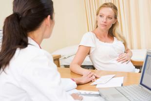 Ein medizinisches Gespräch zwischen einer Ärztin und einer schwangeren Patientin, wobei die Ärztin ein Klemmbrett in der Hand hält und die Patientin ein weißes Oberteil trägt.