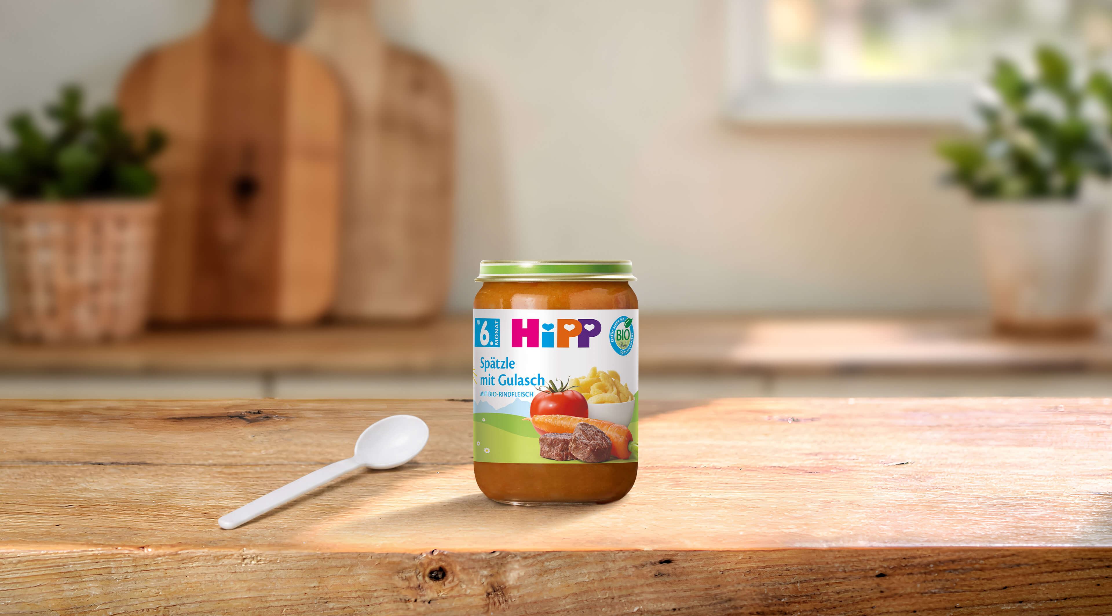 HiPP Bio Babygläschen Spätzle mit Gulasch 190g ab 6. Monat auf Holztisch mit Löffel in heller Küche