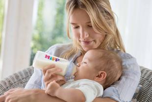 Mutter füttert ihr Baby liebevoll mit einer HiPP Flasche mit Folgemilch im hellen, gemütlichen Wohnzimmer.