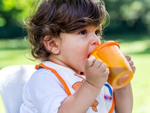 Ein kleines Kind, vermutlich ein Kleinkind, nippt im Freien an einer orangefarbenen Schnabeltasse.