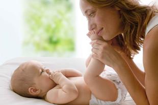 Ein zärtlicher Moment zwischen einer Mutter und ihrem Baby, in dem die Mutter sanft die Füße des Babys hält und die beiden sich tief in die Augen schauen.