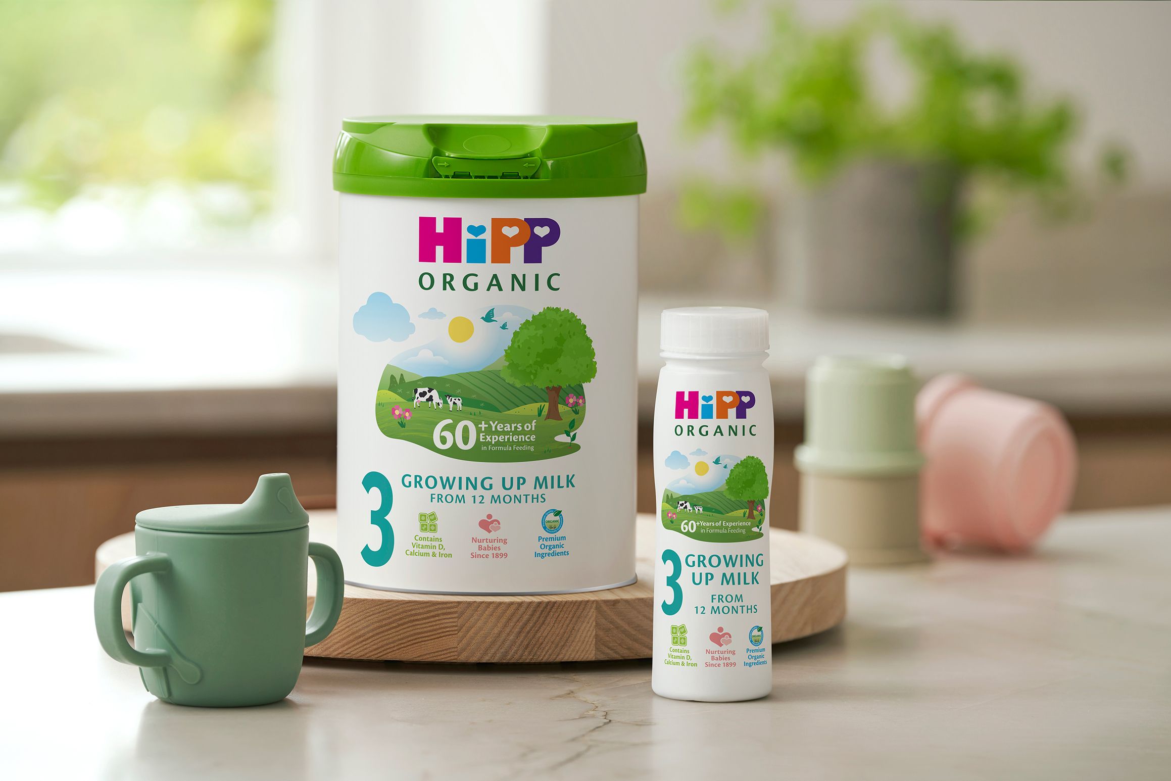 HiPP Organic growing up milk tub and ready-to-feed bottle on a kitchen counter beside a green toddler beaker