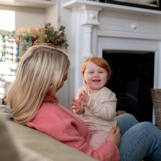 Baby set on mums lap in lounge clapping her hands