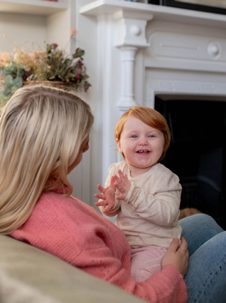 Baby set on mums lap in lounge clapping her hands