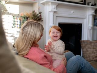 Baby set on mums lap in lounge clapping her hands